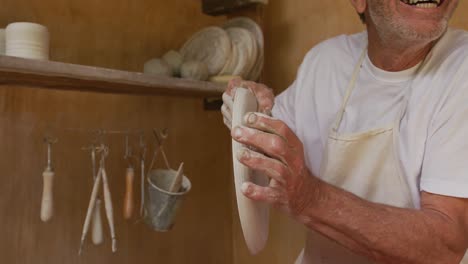 Senior-caucasian-man-wearing-apron-and-making-pottery-in-his-workshop