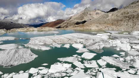 Spinning-aerial-flyover-above-a-glacier-lake-full-of-melted-icebergs-in-remote-parts-of-the-Swiss-Alps-on-a-sunny-day