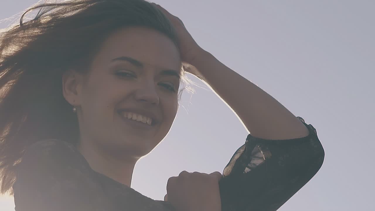 짧은 머리카락을 가진 행복한 소녀가  ⁇ 빛에 맞서 바람에 흔들리고 있습니다.