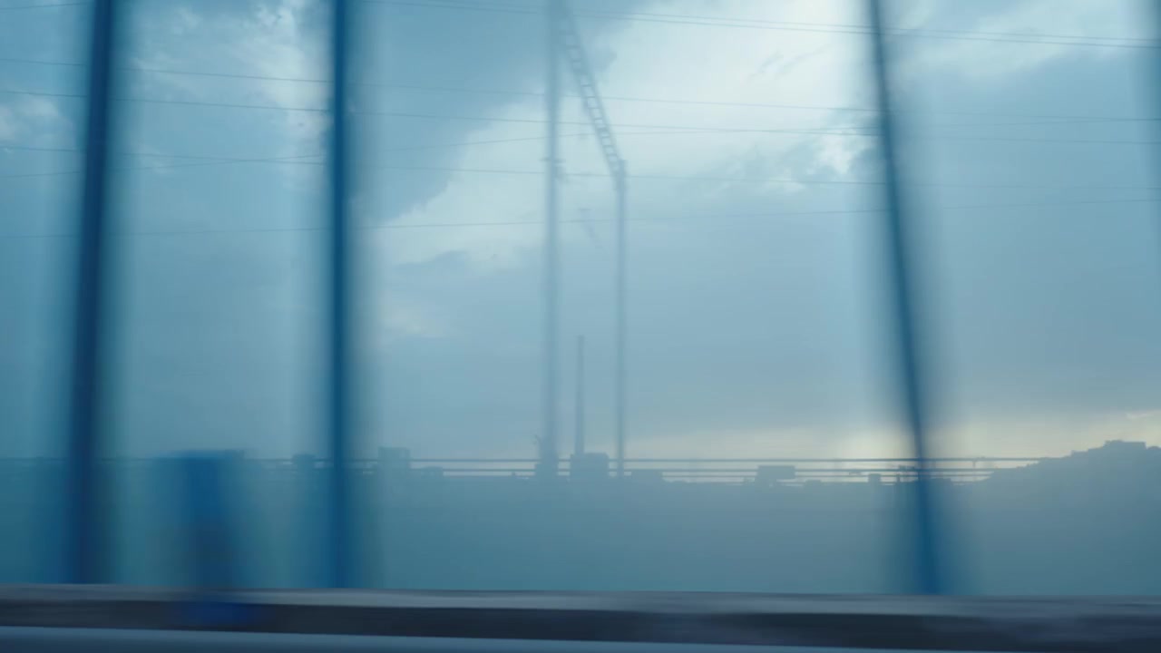View through transparent sound barrier while driving, urban roadside landscape visible.