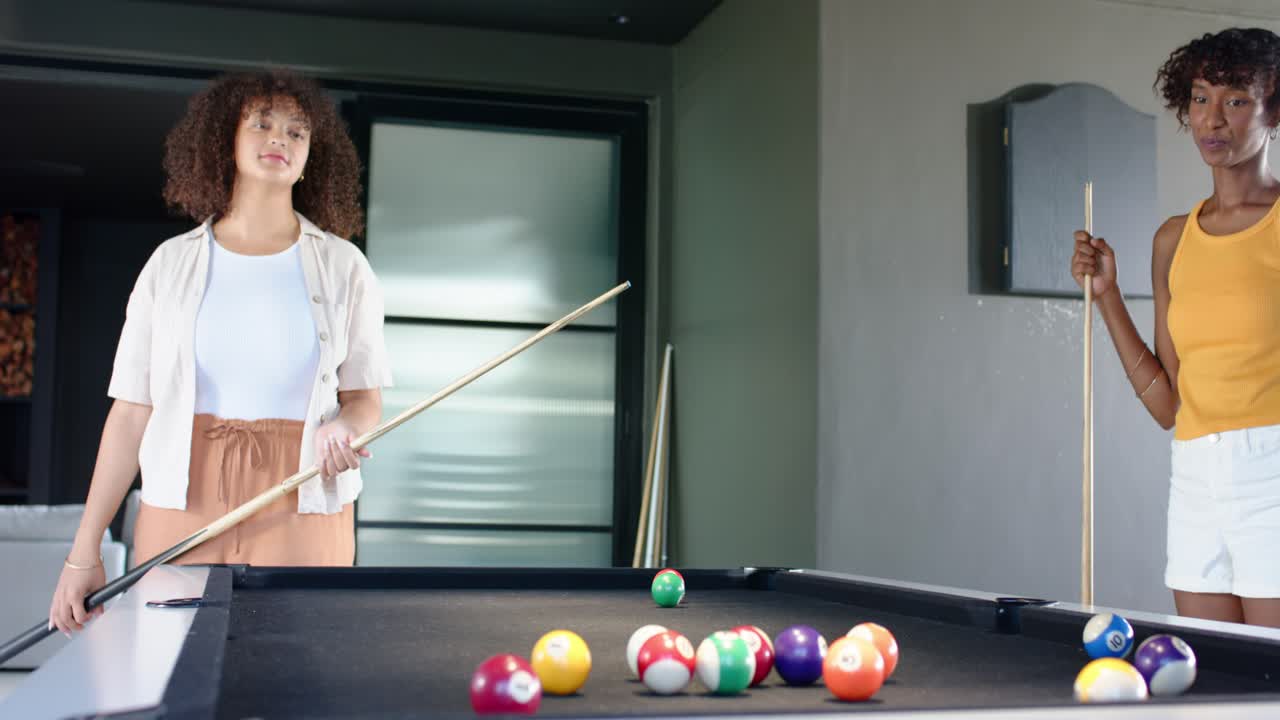 Afro-Amerikaanse vrouwen aan een pooltafel thuis, een vrouw die een cluster van ballen aanwijst, de keu richt en ballen afstoot die in de pockets vallen.