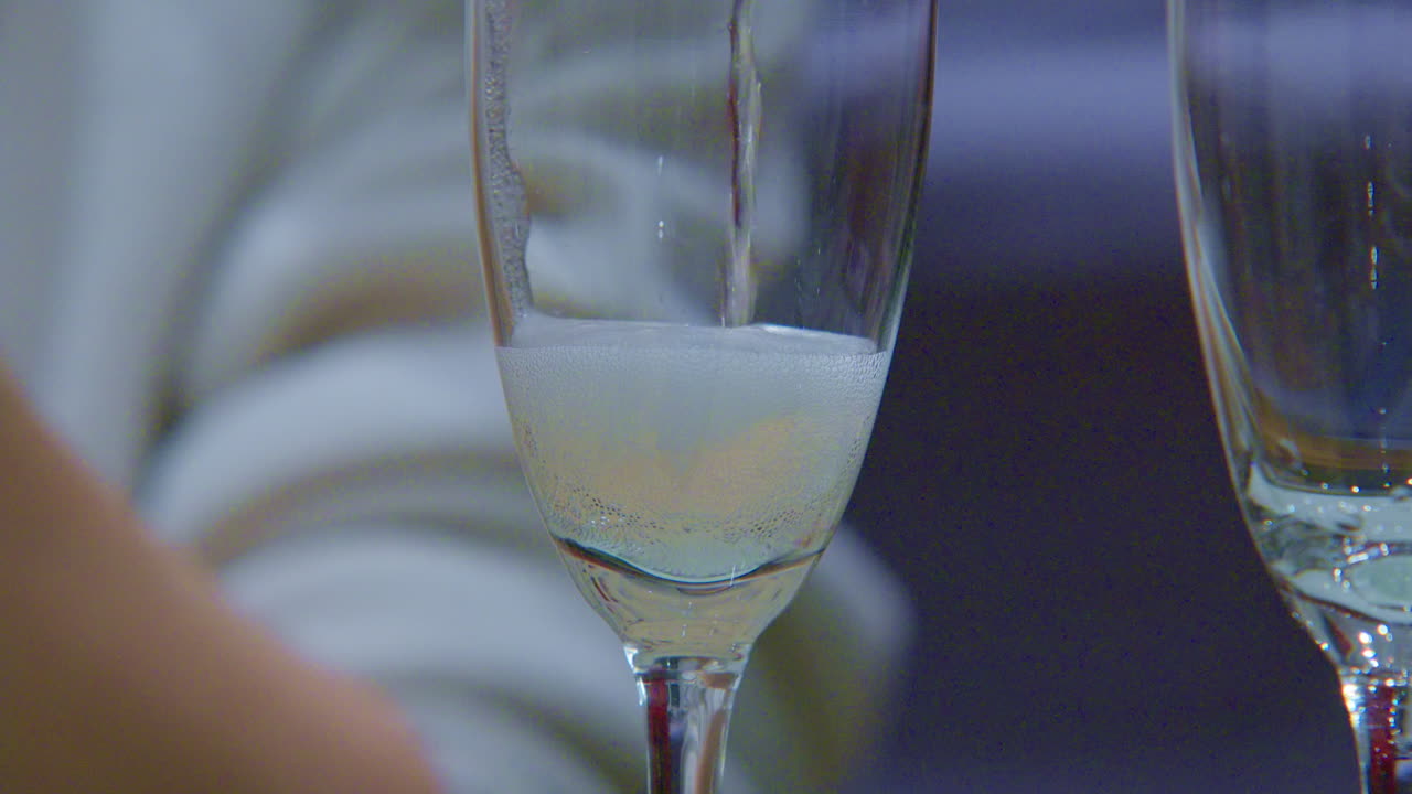Versamento di champagne, bevanda frizzante e gassata con bollicine, da una bottiglia in un bicchiere, vista ravvicinata.