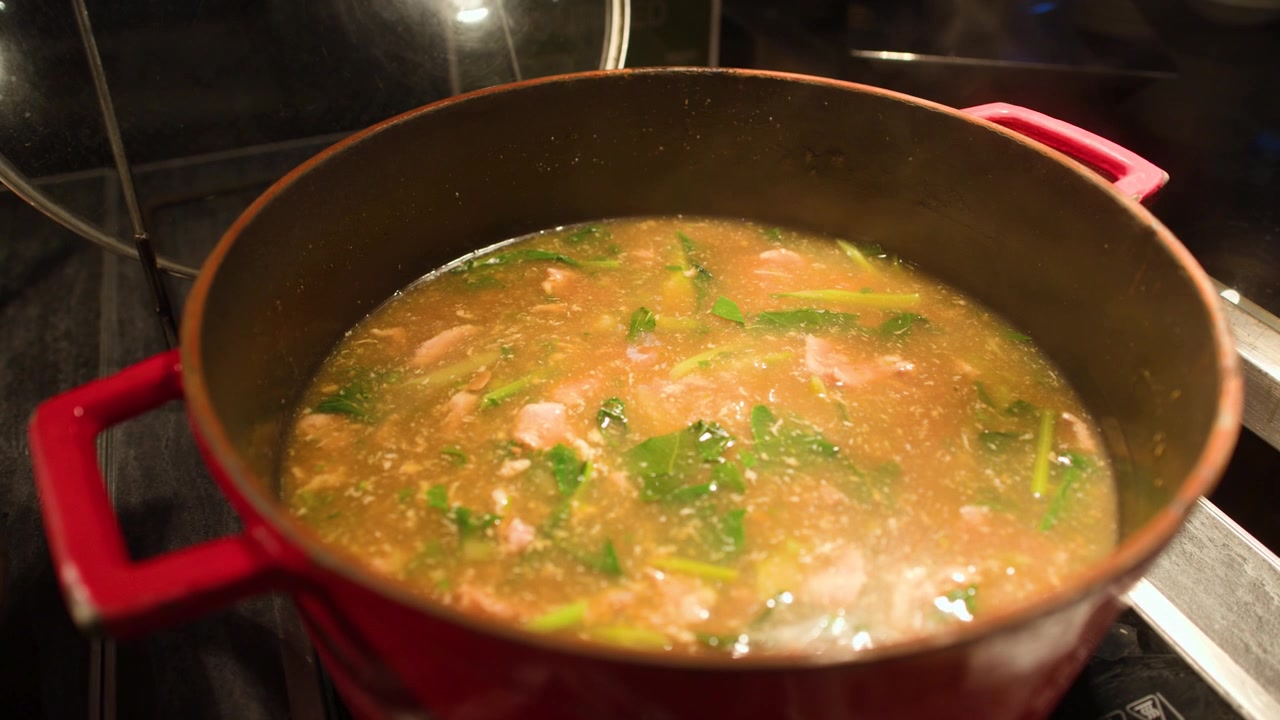Una pentola di ghisa rossa contiene zuppa di pesce thailandese fumante con erbe fresche e gamberi