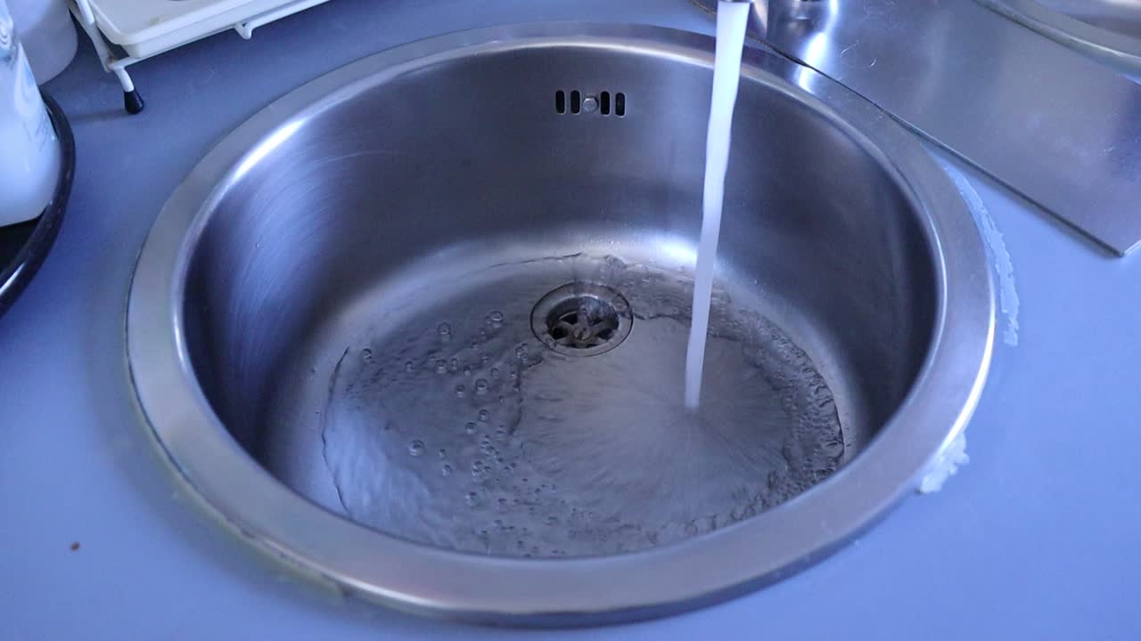Fresh running water flowing into a clean stainless steel kitchen sink with bubbles forming around the drain.