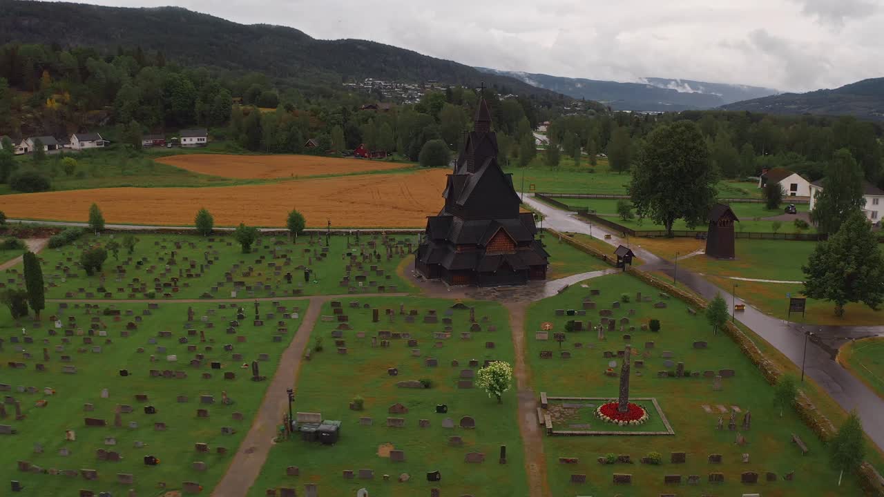 A norwegian church surrounded by a cemetery and scenic landscape, aerial view