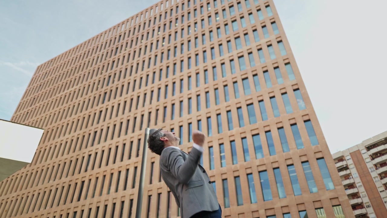 Empresário animado celebra sucesso com telefone em frente a edifício moderno
