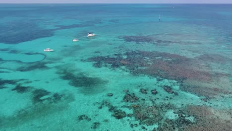 a 4k drone shot of boats floating in crystal-clear blue water of the caribbean sea, near bimini, bahamas