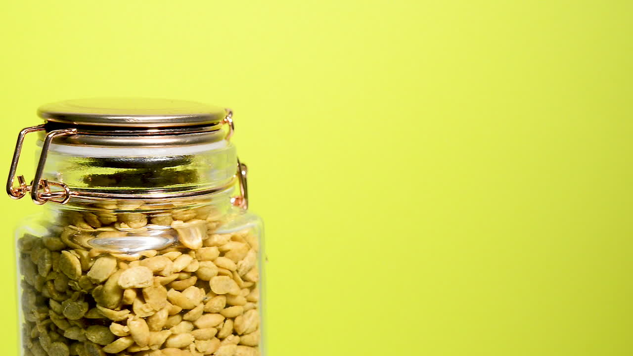 detalle de un tarro de albañil hermético que gira con mitades de soja tostadas secas sobre un fondo lila neón