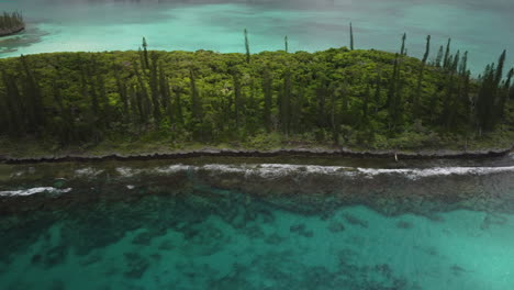 aerial tracking shot past small island near isle of pines, reveal of n'ga peak in background