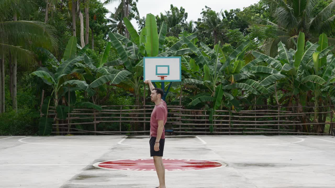 hombre imitando un tiro de baloncesto en una cancha al aire libre con exuberante vegetación en el fondo, filipinas