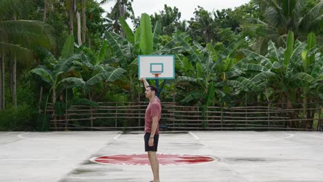 Man-miming-a-basketball-shot-on-an-outdoor-court-with-lush-greenery-in-the-background,-Philippines