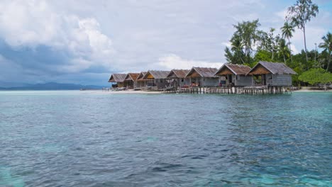 Traditional-stilt-huts-line-the-turquoise-waters,-with-lush-greenery-and-a-dramatic,-cloudy-sky-in-the-background