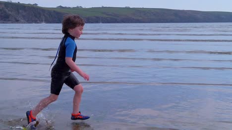 A-wide-shot-of-a-young-boy-running-parallel-to-camera-across-beach-surf-on-a-fine-day