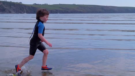 a wide shot of a young boy running parallel to camera across beach surf on a fine day