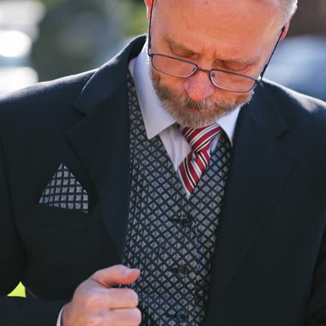 serious businessman wearing eyeglasses talks on phone while looking at camera. portrait of a senior man in suit and tie talking on a cell phone in the city.