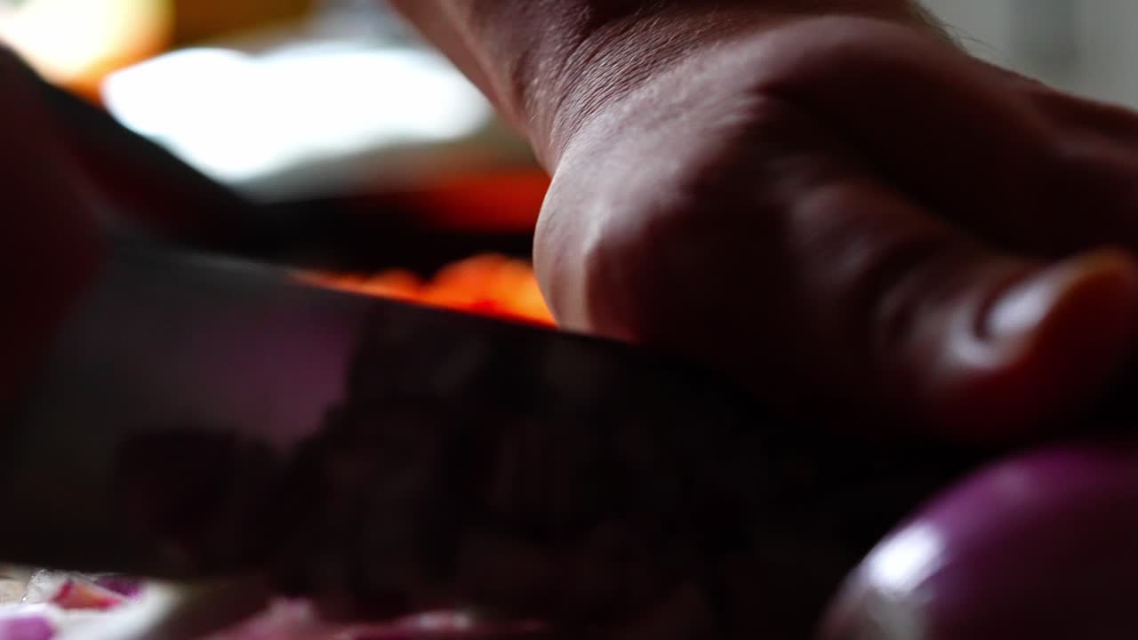 Close of sharp knife slicing red onion cleanly, purple layers separate on board