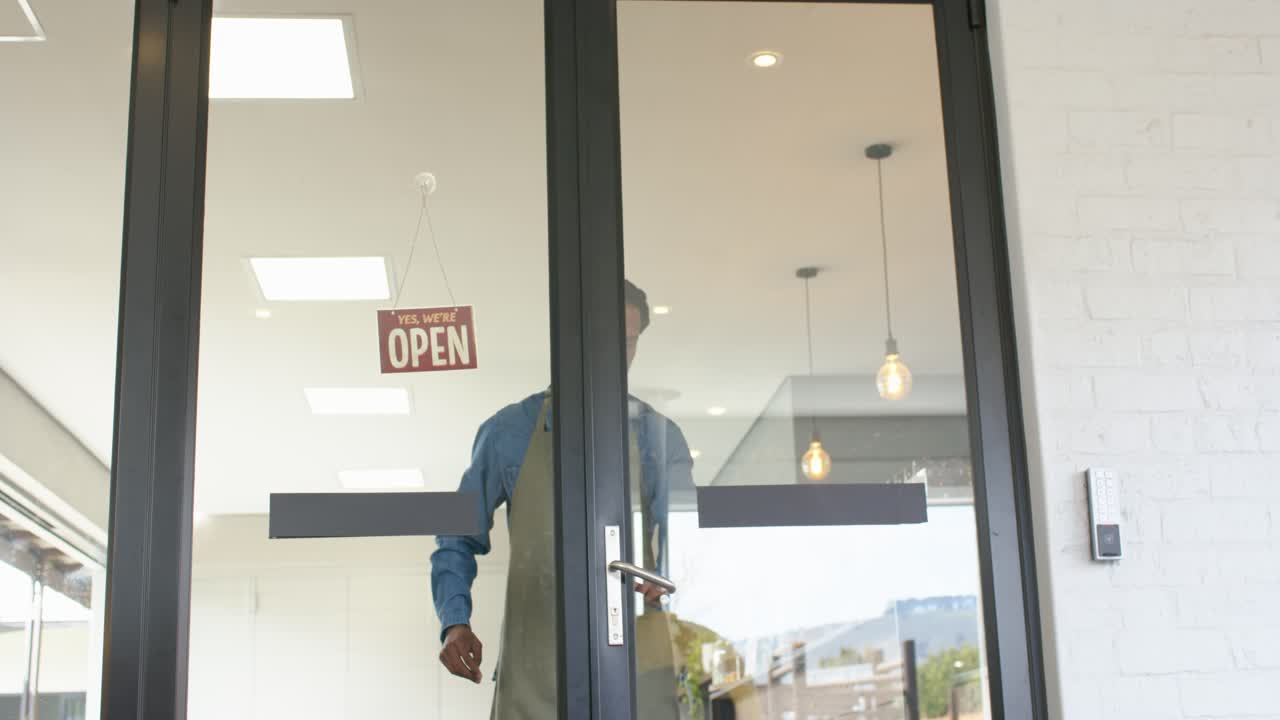 African American man flipping closed sign and unlocking glass door, stepping outside opening shop