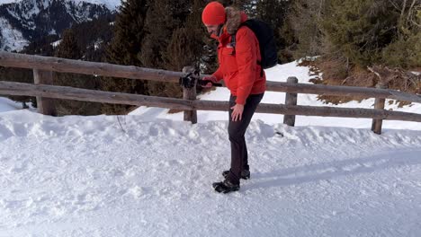 Videographer-with-red-snow-jacket-and-hat-using-professional-camera-mounted-on-stabilizing-gimbal-DJI-RS-3-Mini-surrounded-by-snowy-mountain-landscape