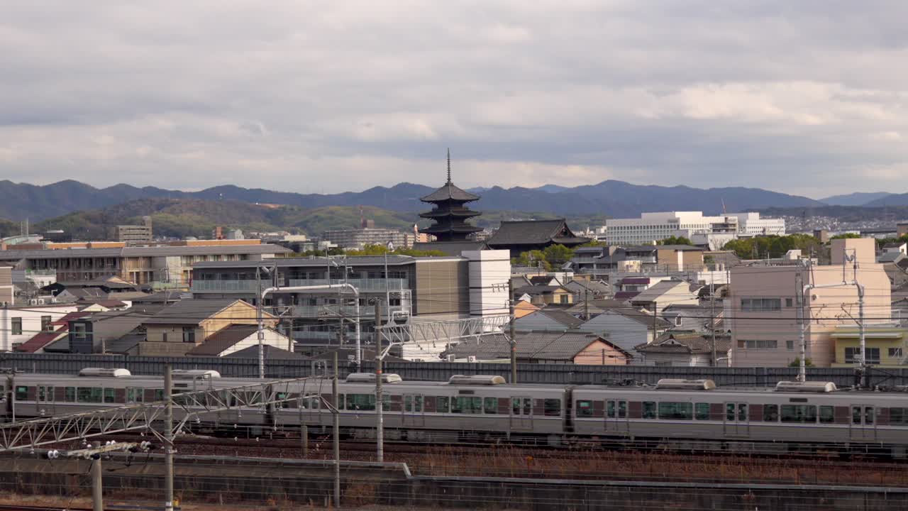 日本の京都鉄道博物館からの眺めを捉えた静止画。線路が写り、京都駅に向かう軽快な列車、そして遠くには象徴的な東寺の五重塔が見える。