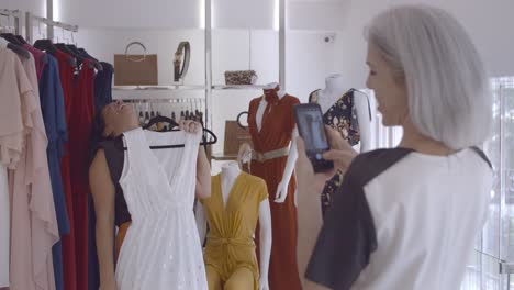 joyful latin woman choosing clothes in fashion store while her friend photographs her