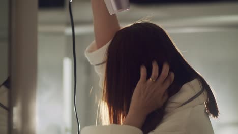 brunette woman wearing bathrobe blow drying hair in bathroom in slow motion