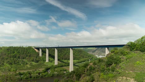 Time-lapse-shot-of-traffic-on-Moselle-Bridge-during-sunny-and-cloudy-day-surrounded-by-green-forest-trees