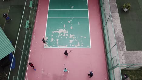 drone footage of some people playing tennis in an old playground against the wall called fronton