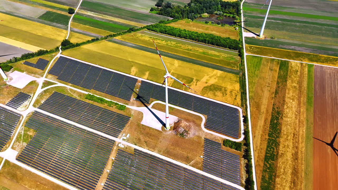 Renewable energy. Wind turbines stand tall amidst extensive solar fields in a vibrant agricultural landscape during daylight