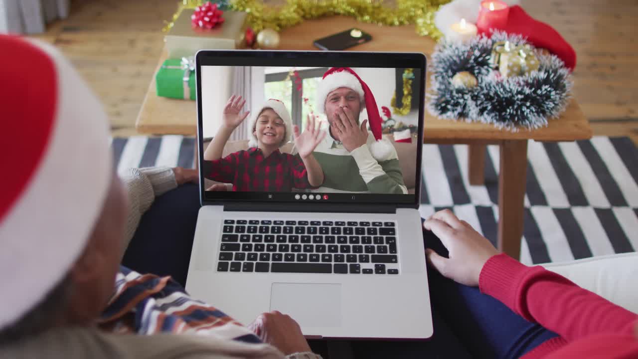 madre y hija afroamericanas usando una computadora portátil para una videollamada de navidad con la familia en la pantalla