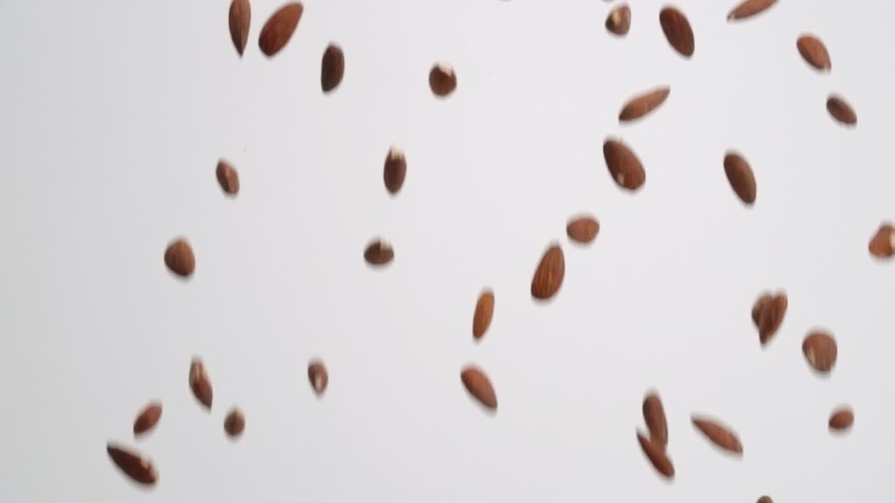 Whole, raw almond nuts raining down on white backdrop in slow motion