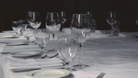 dining table set for a wedding or corporate event at fine dining restaurant ceramic plates forks knives cloth napkins on white tablecloth on table steady slow motion tilting right