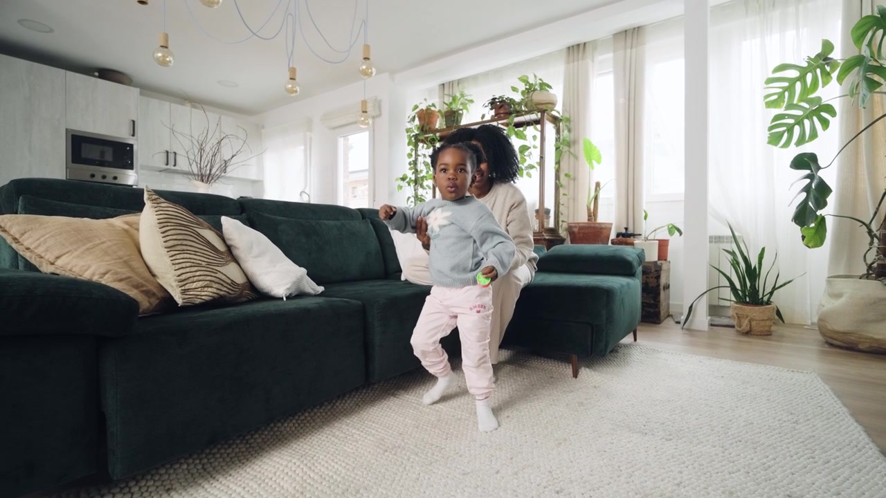 Happy Mother Helps Toddler Daughter Learn to Walk in Living Room