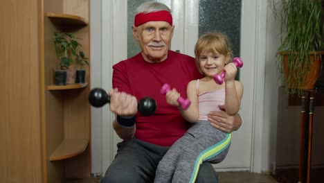 child kid girl with senior grandfather in sportswear making sports workout exercises with dumbbells