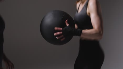 studio shot of two mature women wearing gym fitness clothing training with weighted medicine ball together