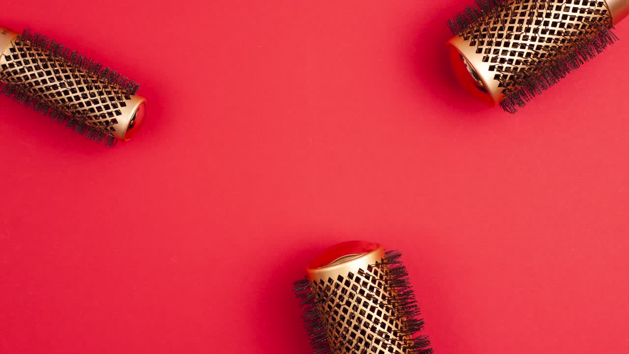 Stop motion animation flat lay from above set of professional gold round hair brushes for styling template with copy space on red background. Hairdresser salon equipment concept, premium set