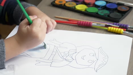 a medium close up of a child at a desk, colouring in a pre drawn figure with watercolour paint