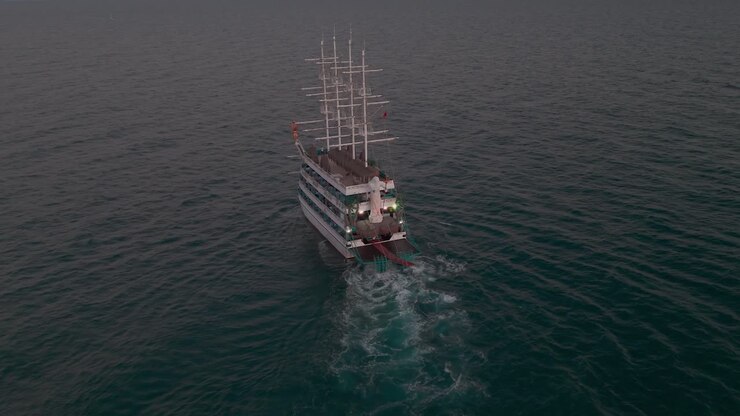 Aerial view following multi level sailing ship with masts leaving wake trail across sunset Mediterranean sea