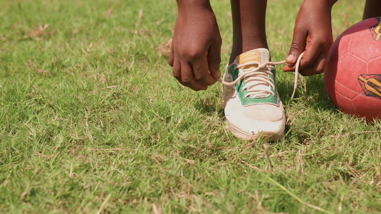 Giovane prepara le calzature. Bambino allaccia le scarpe sull'erba. Campo immacolato mentre il giovane giocatore si prepara per la partita. Giovane appassionato di sport concentrato allaccia le scarpe su campo erboso prima di iniziare a giocare.
