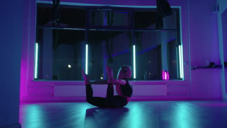 una mujer baila en un estudio con una luz de neón realizando ejercicios y movimientos graciosos de estiramiento y baile en cámara lenta