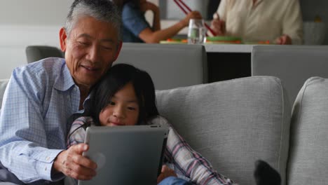 Front-view-of-cute-asian-granddaughter-and-old-senior-grandfather-using-digital-tablet-at-home-4k