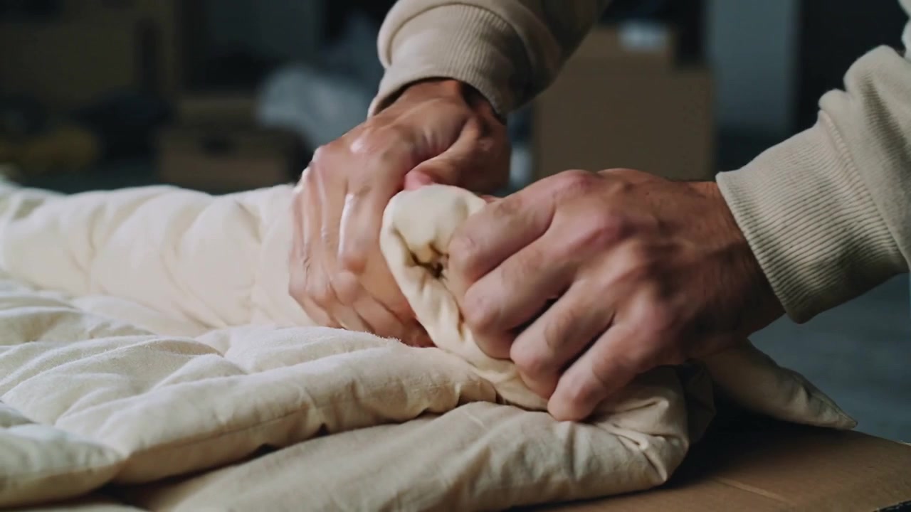 Mani che entrano dall'alto, lisciando, pizzicando e premendo una trapunta su un tavolo, preparandola per l'imballaggio di polsini color cuoio.