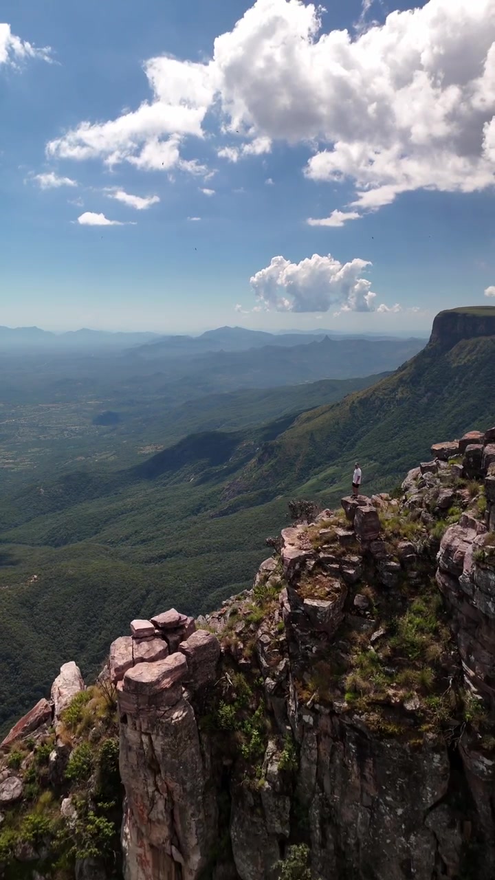 Tomada aérea deslumbrante de dramáticos pilares de rocha na Fenda da Tundavala com uma pessoa em pé na beira de um penhasco com vista para um vasto vale em Lubango, Província da Huíla, Sul de Angola
