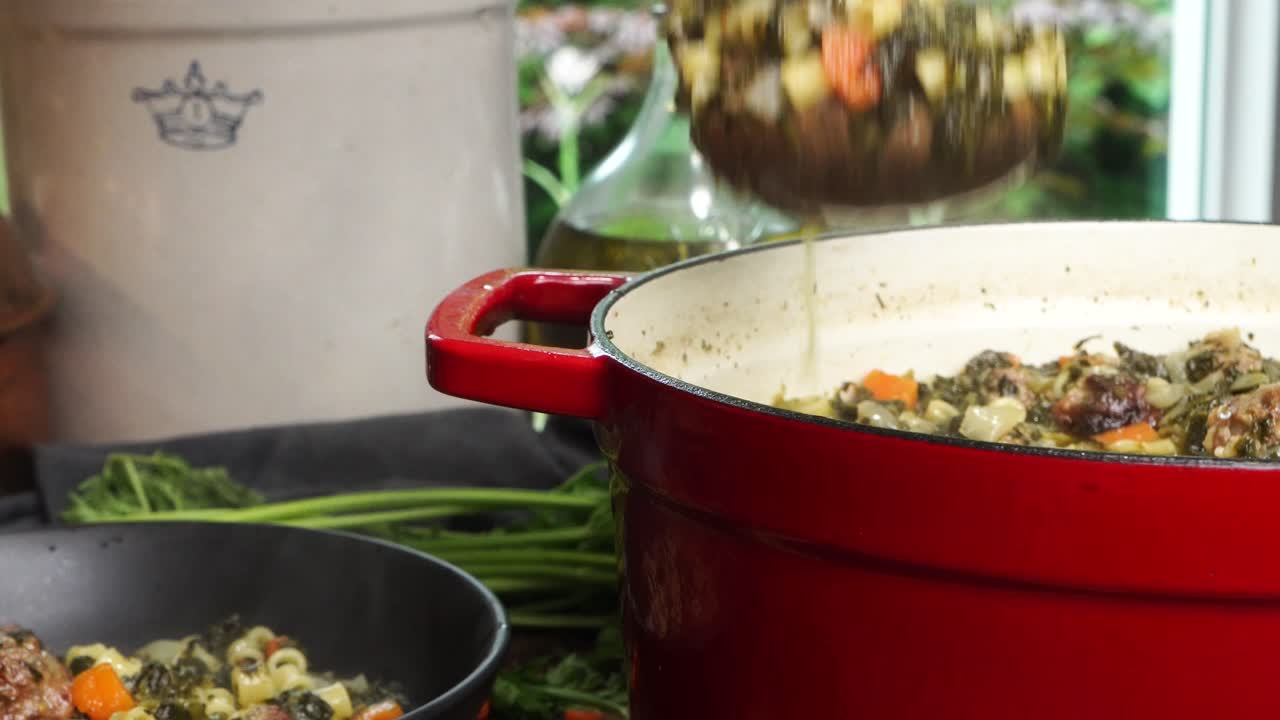 Close up of getting a wooden spoonful of Italian Wedding soup from the red stock pot to a black bowl. Filling a black ceramic bowl with homemade soup with pasta and meatballs and topped with cheese.