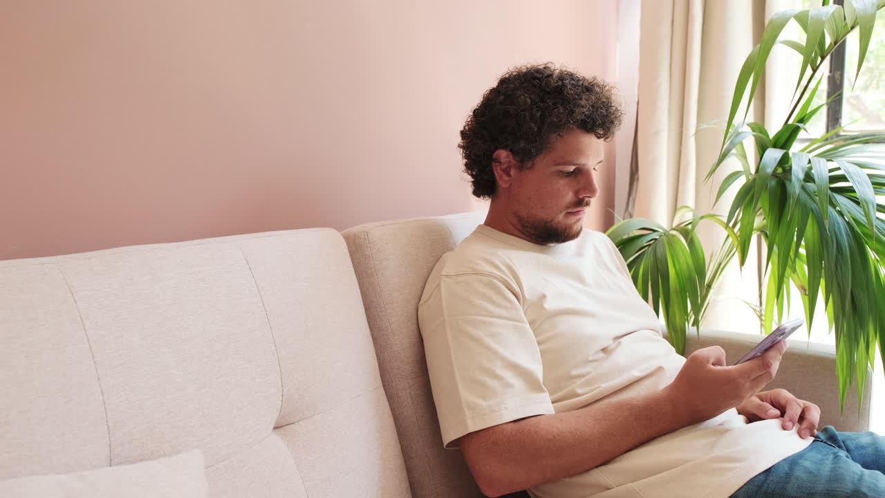 Young Man Sitting on Couch and Using Smartphone at Home