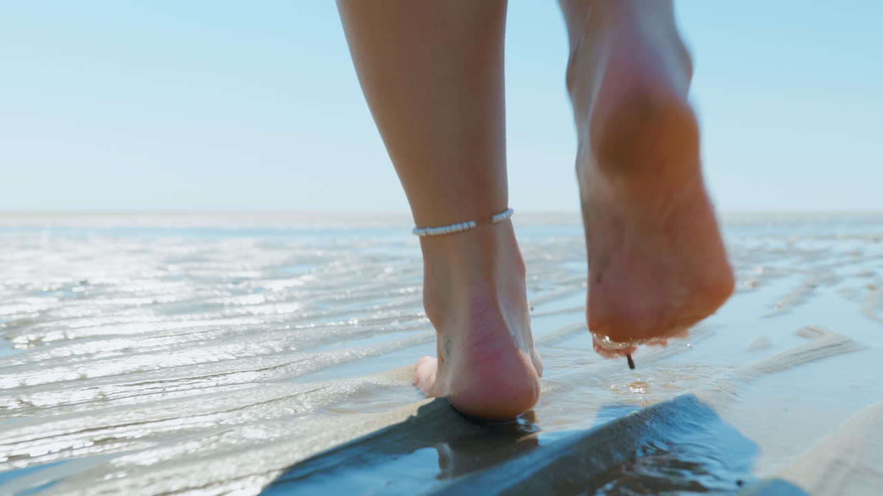 Close up of woman's feet walking across sand