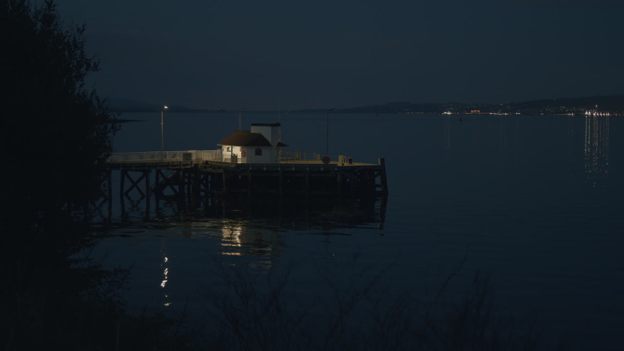 старый деревянный пирс в вечернем свете, с водой и далекими мигающими огнями, статический широкий с деревьями вокруг