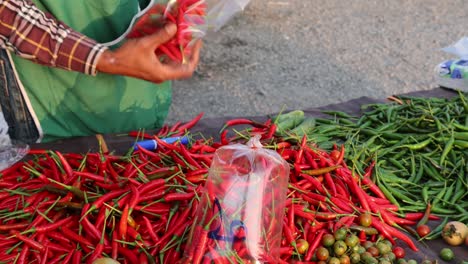 person swiftly bagging red chilies at a market stall