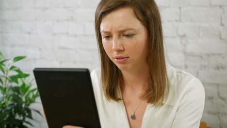 A-happy-young-woman-using-a-tablet-sitting-at-a-desk