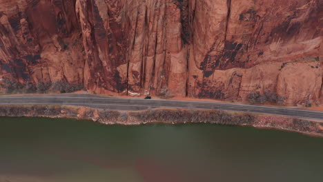 aerial view, dark vehicle parked by the road by colorado river and steep cliffs of utah desert, tilt down drone shot