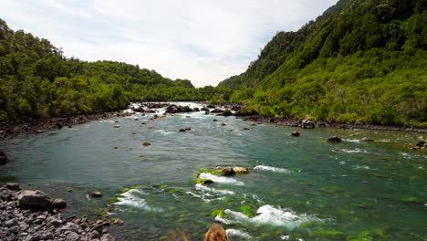 couple standing on volcanic sandbank, admiring scenic petrohué river flows through lush green forest, chile. aerial forward overhead